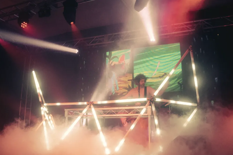 Electronic music producer Luke Million performing live on stage surrounded by heavy smoke, stage lighting, and a custom geometric light-tube setup.